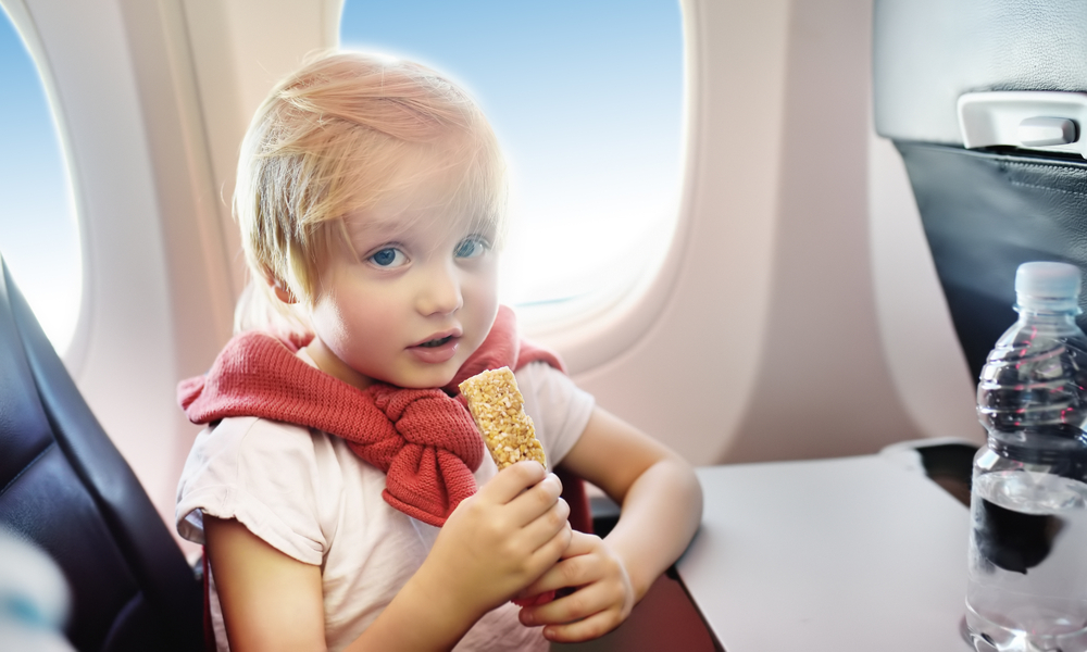 what to pack in your carry-on: Little boy drinking water and eating snack during the flight. 