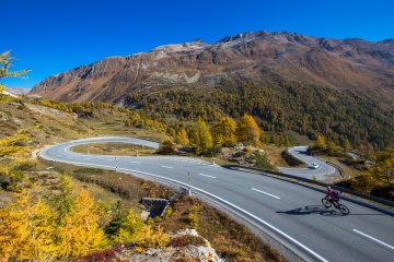 Mountain road in Switzerland. Bernina mountain pass street on a beautiful autumn day. Road through the alps in Europe. Fantastic sunny day for a road trip with a car. Cyclist on a curved road.