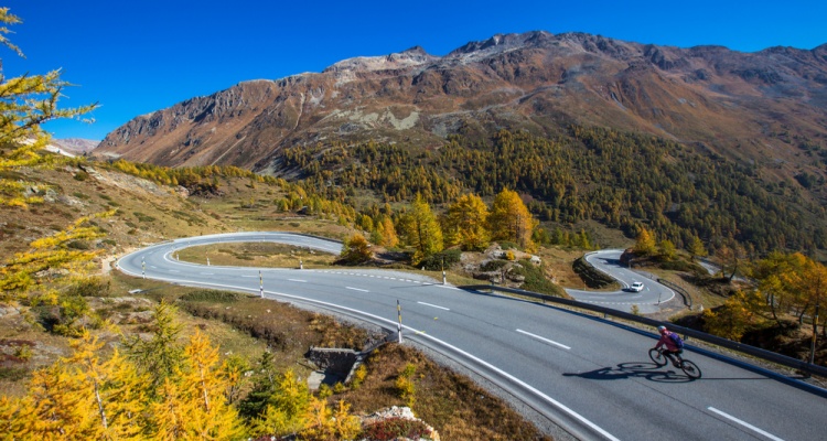 Mountain road in Switzerland. Bernina mountain pass street on a beautiful autumn day. Road through the alps in Europe. Fantastic sunny day for a road trip with a car. Cyclist on a curved road.