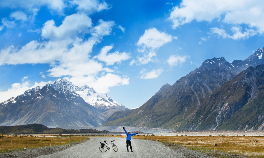 A mountain biker is on the winding gravel track in a valley among fields on a background of blue sky with clouds