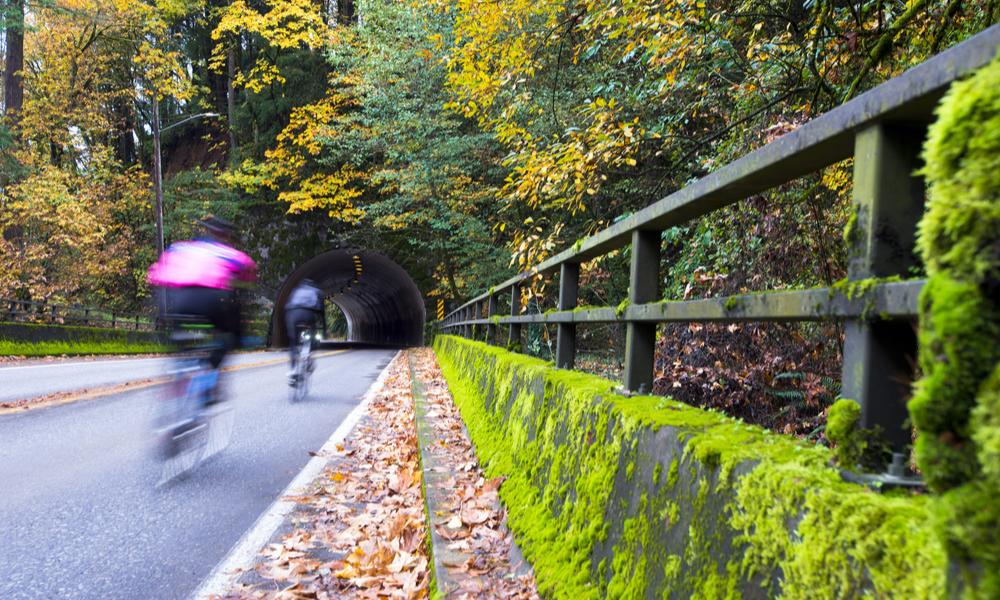 Cyclists rapidly moving toward an arched tunnel, carved into the rock, 