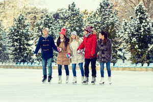 people, winter, friendship, sport and leisure concept - happy friends ice skating on rink outdoors