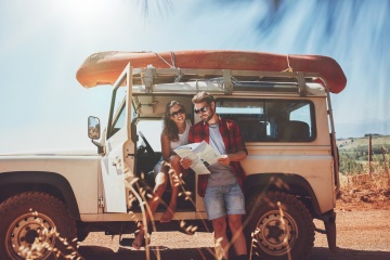 Young couple taking a break to look at a map while on a roadtrip. Young man and woman on country road looking for directions on map.