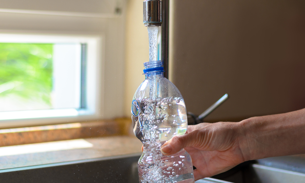 Woman filling a plastic bottle with water from the faucet