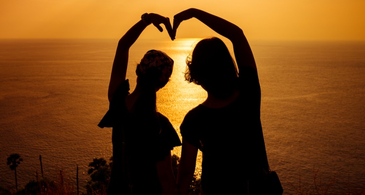 Silhouette photo of two girls arranged their arms in heart shape with sunset background