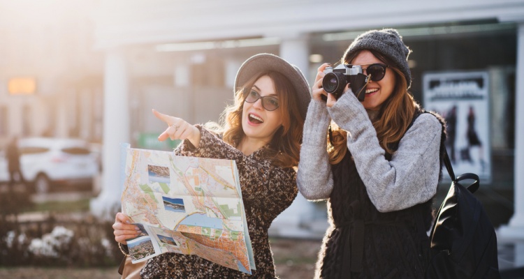 Happy travel together of two fashionable girls in sunny city centre. Young joyful women expressing positivity, using map, vacation with bags, camera, making photo, cheerful emotions, great mood