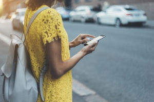 Young hipster girl in yellow dress traveling in Europe and using an app for search local cafe or sightseeing, female hands typing on touch screen of cellphone device to send an sms message