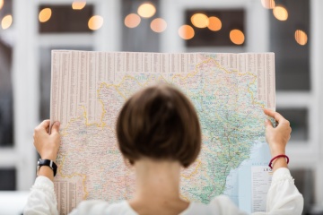 Young beautiful female traveler standing on the street with window and light. Trendy look searching direction on location map while traveling abroad.