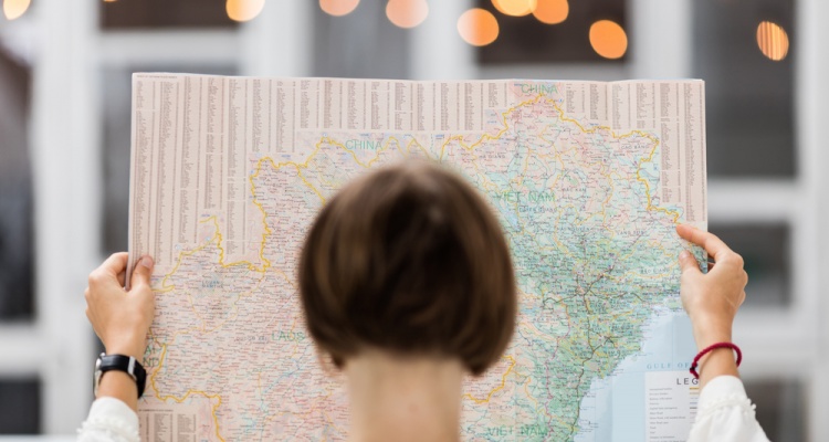 Young beautiful female traveler standing on the street with window and light. Trendy look searching direction on location map while traveling abroad.