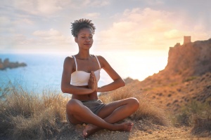 Beautiful woman doing yoga on a cliff, behind an amazing sunset in the sea