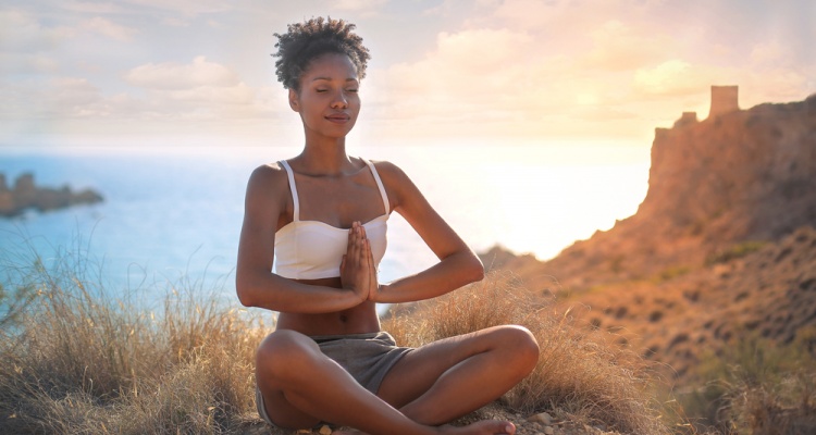 Beautiful woman doing yoga on a cliff, behind an amazing sunset in the sea