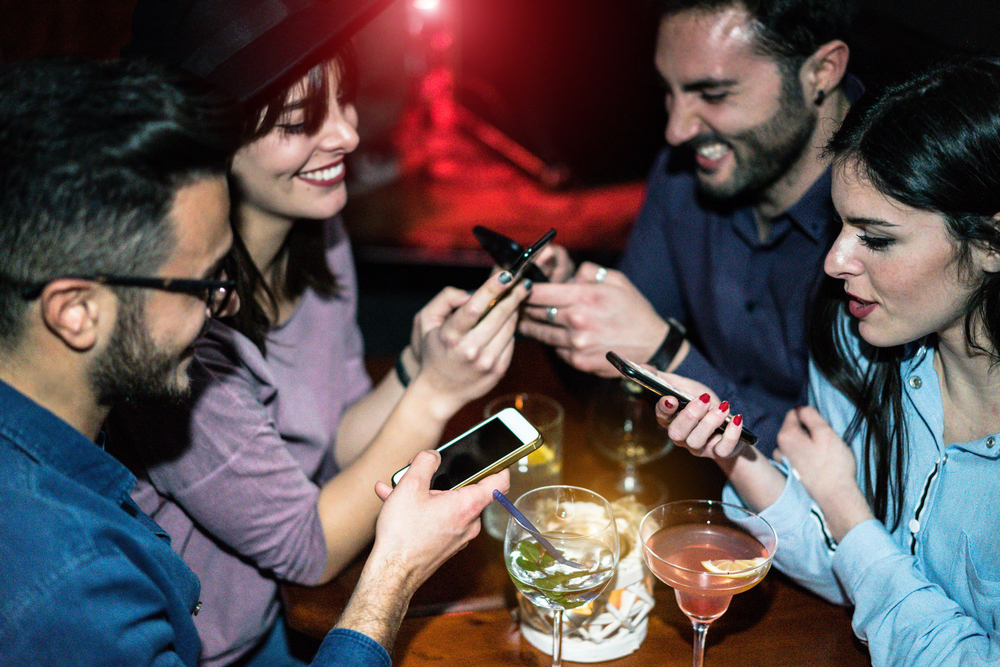 Happy friends using mobile phones in jazz cocktail bar - Young people are addicted to new trends technology - Online social concept - Focus on right girl face - Unfiltered photo made with flash