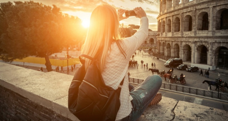 Woman tourist selfie with phone camera in hands near the Coliseum in Rome under sunlight and blue sky. Famous popular touristic place in the world.