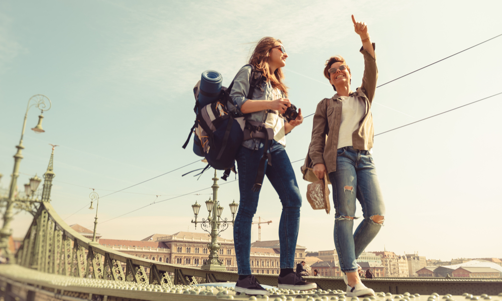 Two young girlfriends traveling, walking on a bridge, enjoying the sunny day and the sightseeing of the city