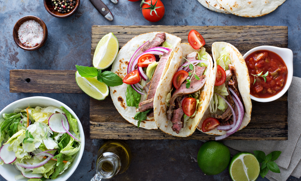 Steak tacos with sliced meet, salad and tomato salsa on a cutting board