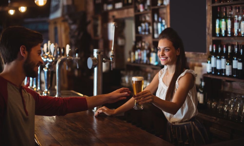 Female bar tender giving glass of beer to customer at bar counter