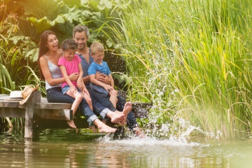 summertime, portrait of an happy family sitting on the edge of a wooden pontoon, feet in the river and making splashes