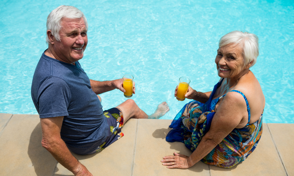 Portrait of senior couple holding juice glasses near poolside