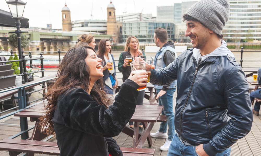 Young couple enjoying a beer at pub in London with more people on background. 