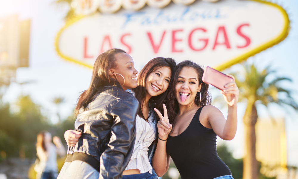 group of friends having fun taking selfies in front of welcome to las vegas sign