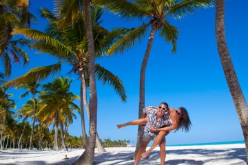 Happy young couple having beach fun piggybacking laughing together during summer holidays vacation on tropical Caribbean beach.