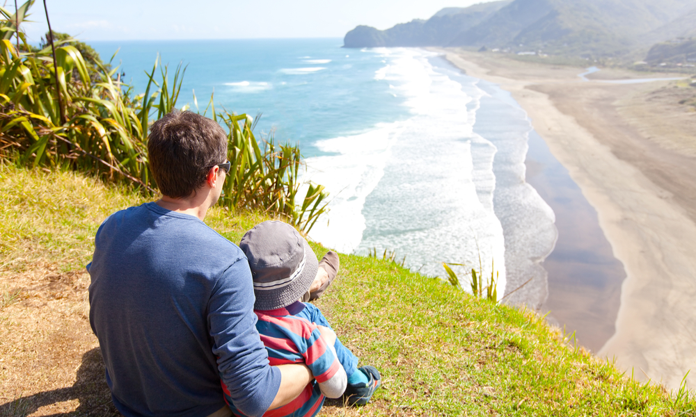  view of family sitting at the top of lion rock at piha beach, new zealand