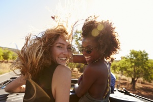 Two women standing in the back of open car turning to camera