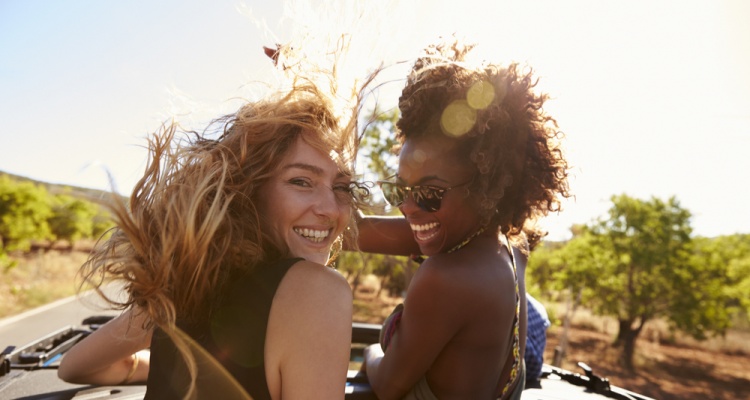 Two women standing in the back of open car turning to camera