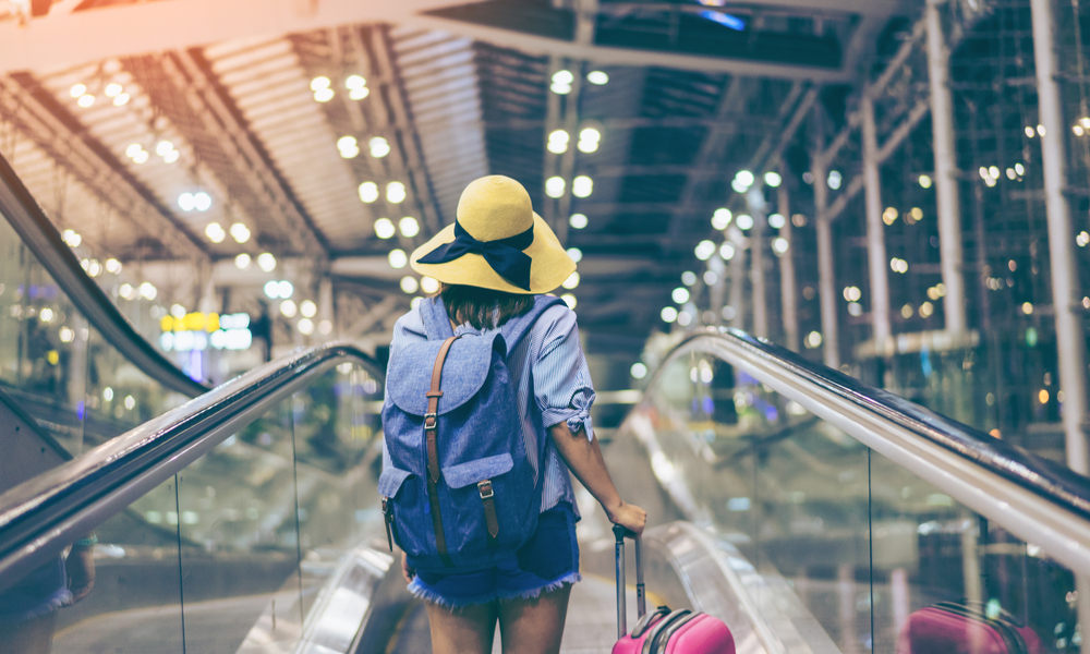 Young woman traveler in international airport with backpack holding suitcase or baggage in her hand