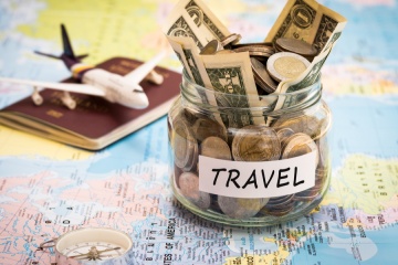 Travel money savings in a glass jar with compass, passport and aircraft toy on world map