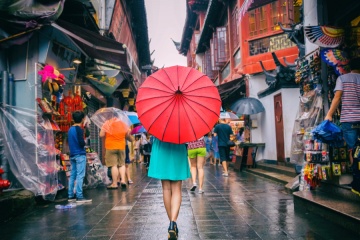 Rainy day girl tourist under red oriental umbrella in narrow alleys on china travel in Shanghai.