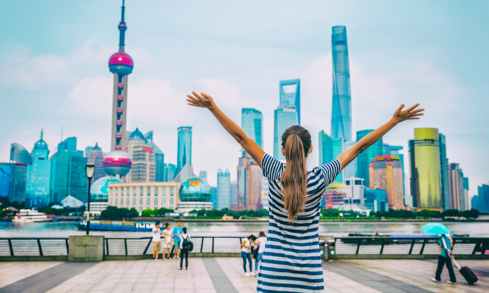 woman with arms up with Shanghai skyline on The Bund.