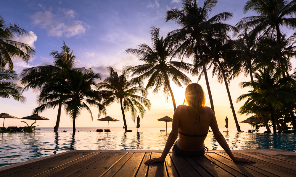 woman sits by poolside at sunset