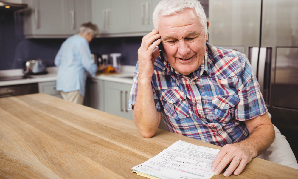 Senior man talking on phone and woman working in kitchen at home