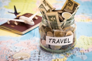 Travel budget concept. Travel money savings in a glass jar with compass, passport and aircraft toy on world map