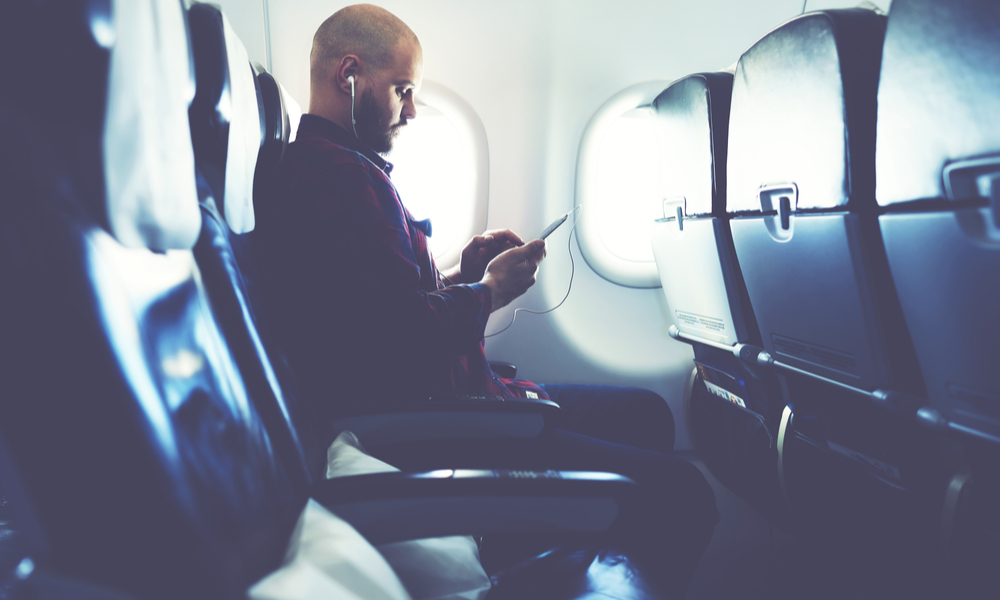 Man is listening to music in headphones and chatting in social network via mobile phone, during his flying in an airplane. 