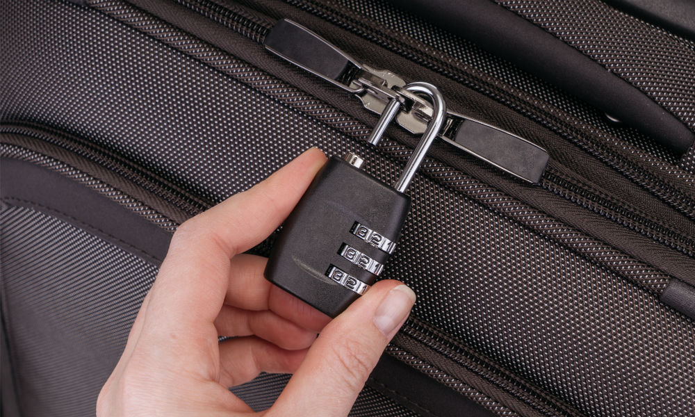 Hand opens suitcase combination lock on the gray suitcase.