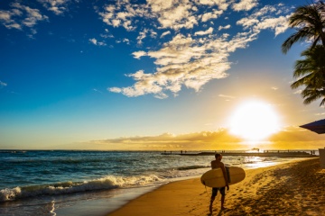 Surfer carrying board with sunset background