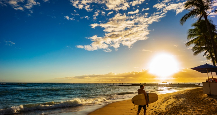 Surfer carrying board with sunset background