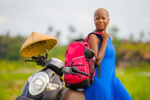 african american woman looking around with scooter motorbike at green field tropical landscape in adventure trip