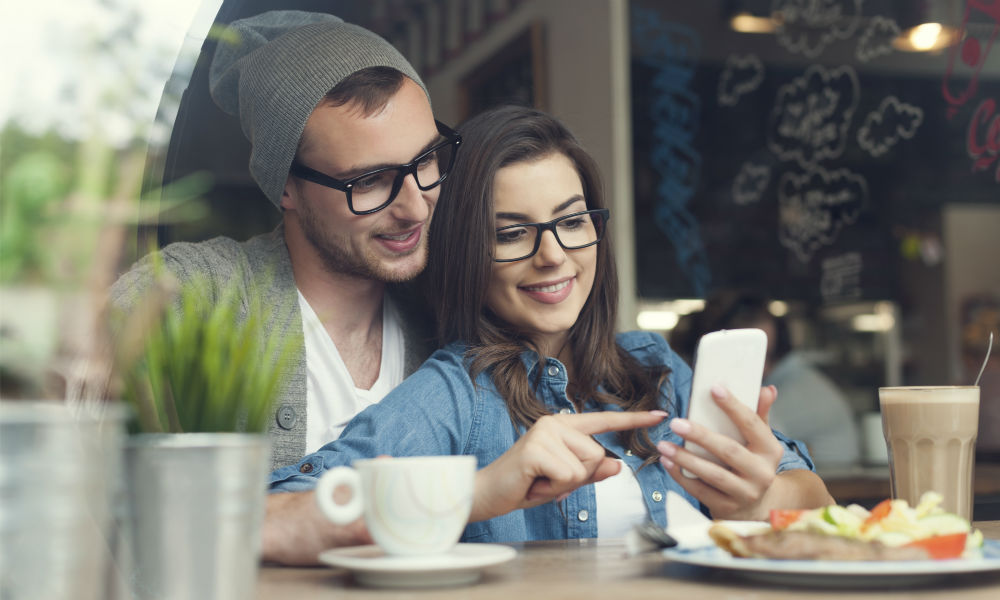 Embracing couple using mobile phone in cafe