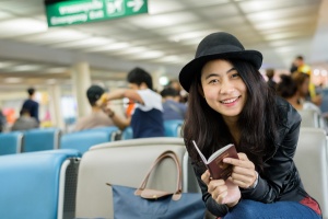 Asian woman solo traveler holding passport and waiting for flight travel at airport terminal