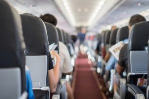 Interior of airplane with passengers sitting on seats and stewardess walking the aisle in background.