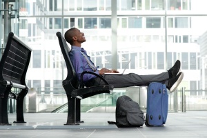 Side portrait of smiling young businessman sitting with laptop and luggage at airport