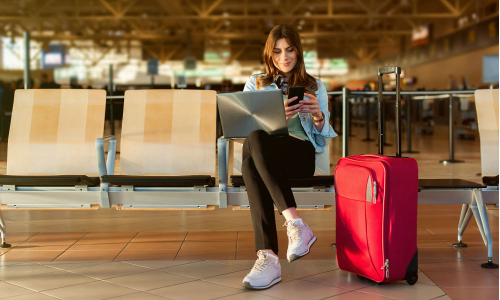 Airport Young female passenger on smart phone and laptop sitting in terminal hall while waiting for her flight