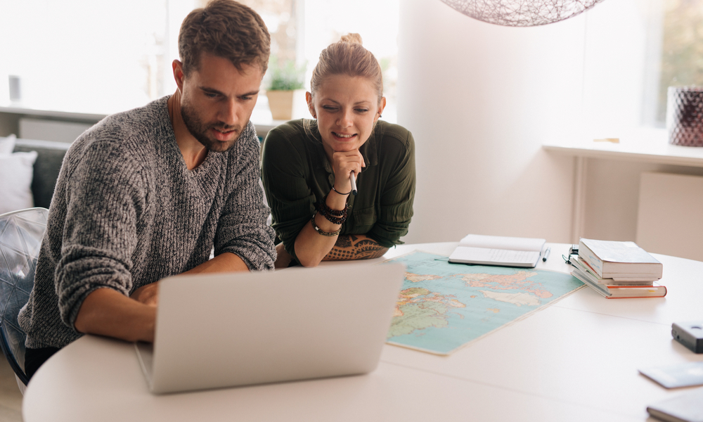 Young man and woman sitting with world map and computer on study table.