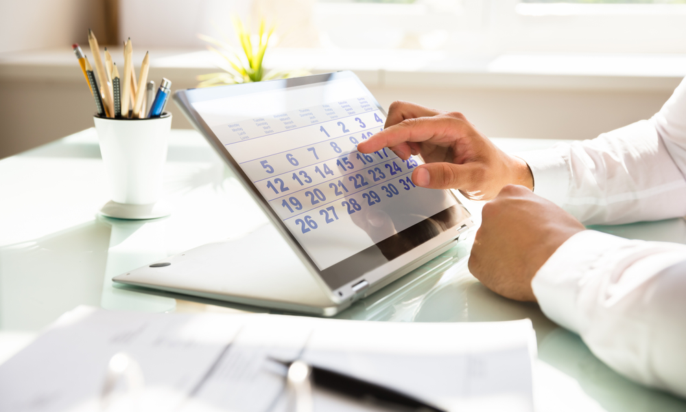 Close-up of a businessman's hand using calendar on laptop over desk