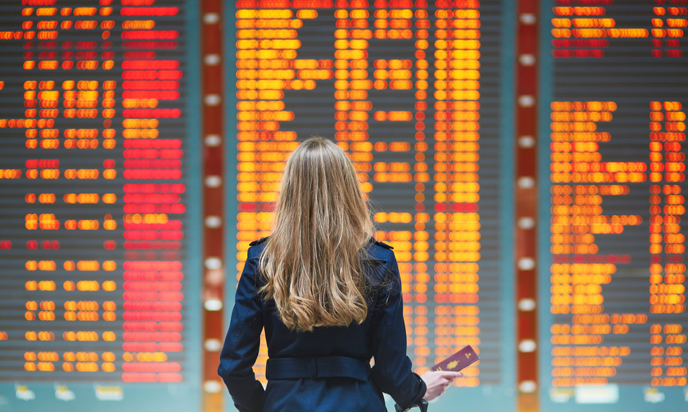 Young woman in international airport looking at the flight information board, checking her flight