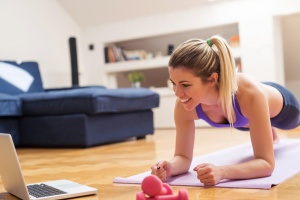 Young girl looking at laptop and doing exercises at home.