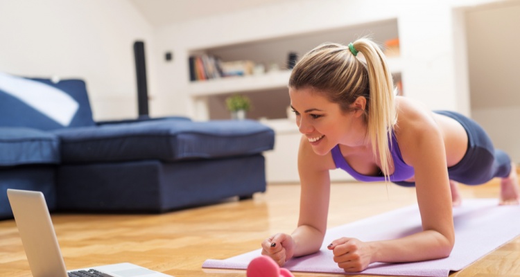 Young girl looking at laptop and doing exercises at home.